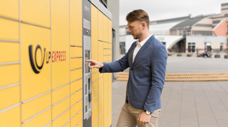 A man wearing a blue hacket and grey trousers collects a parcel a a bank of yellow LX Express parcel lockers.