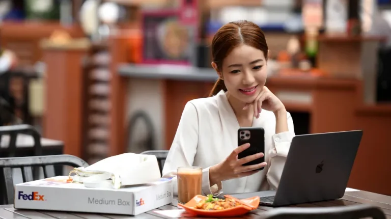 Asian woman looking at cell phone with Fedex package on table