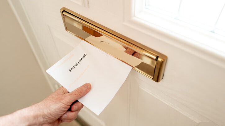 Homeowner seen pulling a UK 2024 Official Polling Card letter through his front door letterbox. The poll card is used to vote in the 2024 UK general election.