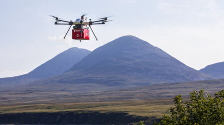 Royal Mail trials drone delivery in Argyll and Bute Drone with red Royal Mail parcel flying over lake with mountains in background