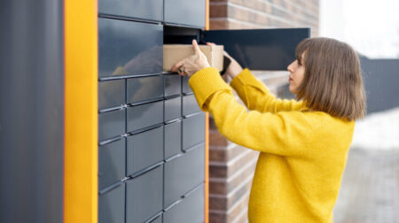 ANALYSIS: Have the number of PUDOs in Europe peaked? Young woman getting parcel from cell of automatic post terminal outdoors. Concept of contactless and smart delivery. Idea of modern shipping and logistics. Woman wearing yellow sweater