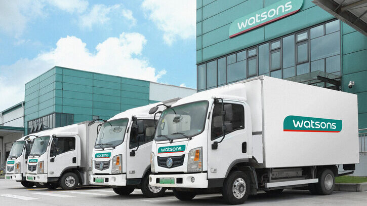 AS Watson boosts sustainability with EV fleet and waste reduction plans White delivery trucks with green Watsons logo on the side, in front of building with blue sky and white clouds in background