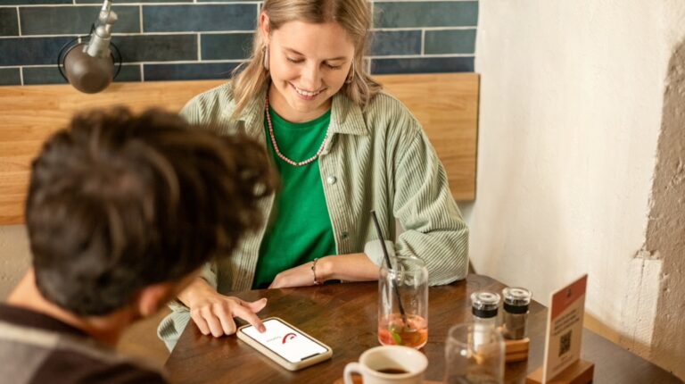 bpost ends physical missed delivery notifications Woman looking at bpost app on her mobile phone while at cafe with man