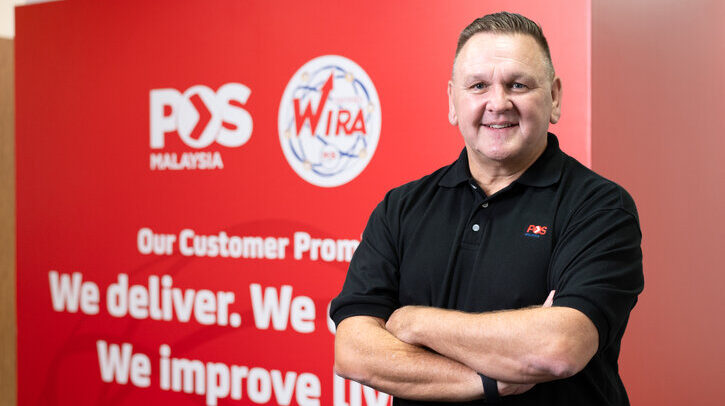 EXCLUSIVE INTERVIEW: Pos Malaysia Charles Brewer, group CEO of Pos Malaysia in black shirt against red Pos Malaysia branded background