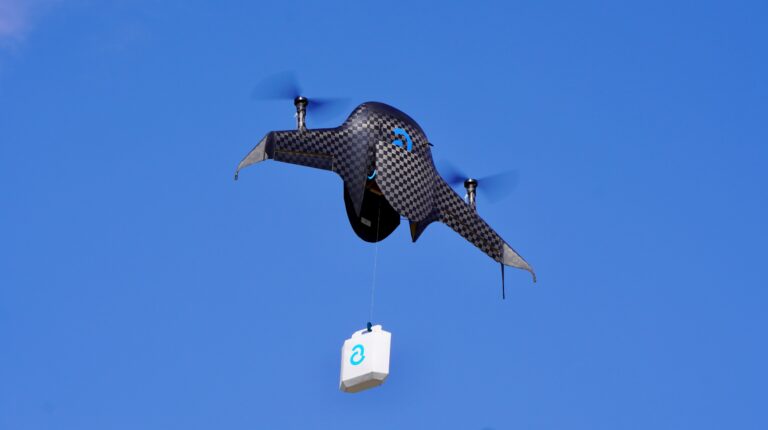 The black Airbound drone in the air with a parcel on a blue sky background.