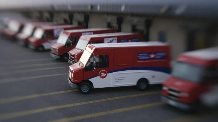 Canada Post reports $841m losses as strike negotiations continue Row of Canada Post red post vans with one pulling out.