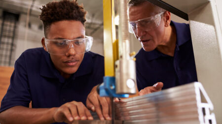Carpenter training male apprentice to use mechanized saw.