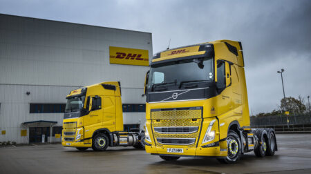 DHL eCommerce UK adds 30 bio-LNG-powered trucks to fleet Two DHL eCommerce trucks sit parked outside a warehouse underneath a grey cloudy sky