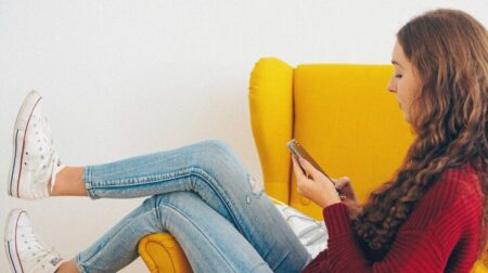 UK and European e-commerce volumes grew 18% in Q2, Scurri reveals A woman in a red jumper and blue jeans reclines on a yellow sofa and looks at her smartphone while make an e-commerce order.