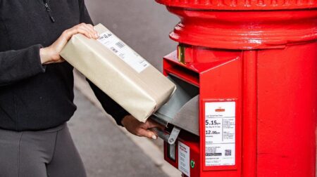 A person puts a small parcel into the new parcel drawer in the new-look Royal Mail postbox