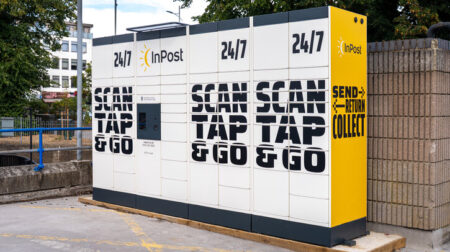 A bank of inPost lockers on a street against a brick wall