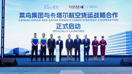 Members of Cainiao and Qatar Airways Cargo stand on a blue stage in front of a backdrop with the company logos on.