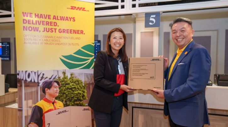 Representatives of DHL and SingPost hold a cardboard box in front of a board with the company logos to mark the announcement of a new partnership to deliver accessible and sustainable shipping services across Singapore