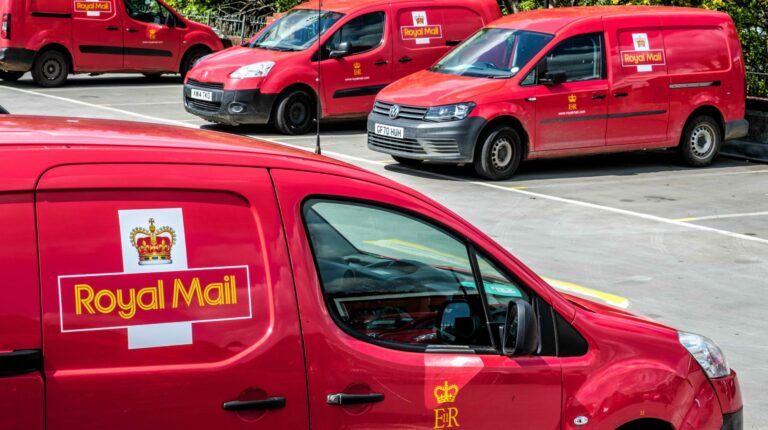 Three-door red Royal Mal delivery vans with the yellow lettering company logo on the side in a parking lot