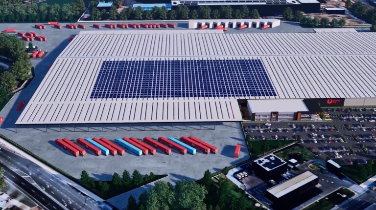 An aerial shot of the former Holden warehouse location in Elizabeth, South Australia, that will be transformed into the new Adelaide Parcel Facility super hub. it has lines of blue and red truck trailers and other vehicles parked outside. and solar panels on the roof