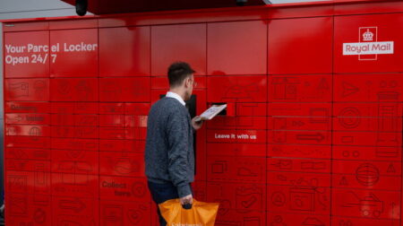 A man collects a parcel at a bank of red Royal Mail lockers