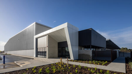 Australia Post opens new parcel facility in Perth The new Australia Post parcel facility in Perth, with a frontage comprising contrasting angles and beams, with a white section and a black section. The sky is blue.