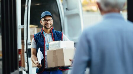 Parcel2Go ranks 2025’s most reliable and trusted UK couriers Happy deliverer carrying packages while making home delivery to his customer.