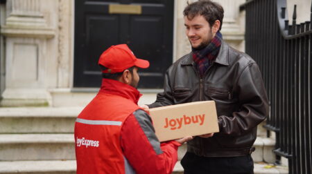 A JD.com employee in a red company branded jacket hands over a parcel to a customer dressed in black.
