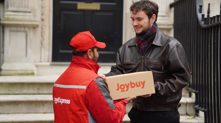 A JD.com employee in a red company branded jacket hands over a parcel to a customer dressed in black.