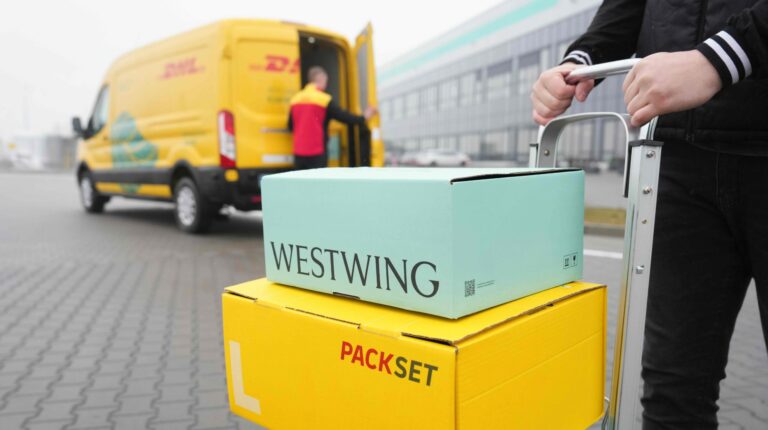A Westwing parcel sits on top of a DHL parcel waiting to be loaded into a yellow DHL delivery van.