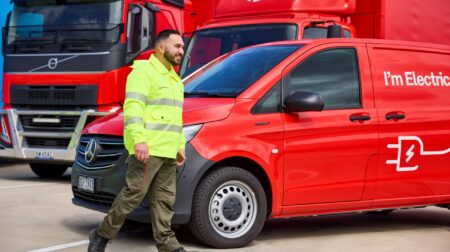 An Australia Post worker in a yellow high-vis jacket walks past an Australia Post delivery van.