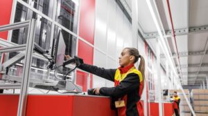 A DHL Supply Chain worker in red, black and yellow branded clothing works in a warehouse facility.