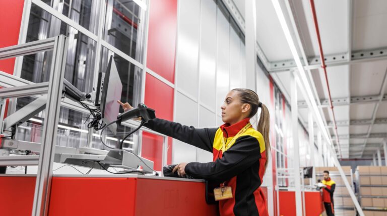 A DHL Supply Chain worker in red, black and yellow branded clothing works in a warehouse facility.
