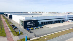 Aerial view of the APL Logistics semi-automated distribution and fulfilment warehouse in the Port of Amsterdam. It has white walls and roof and black doors along the side.