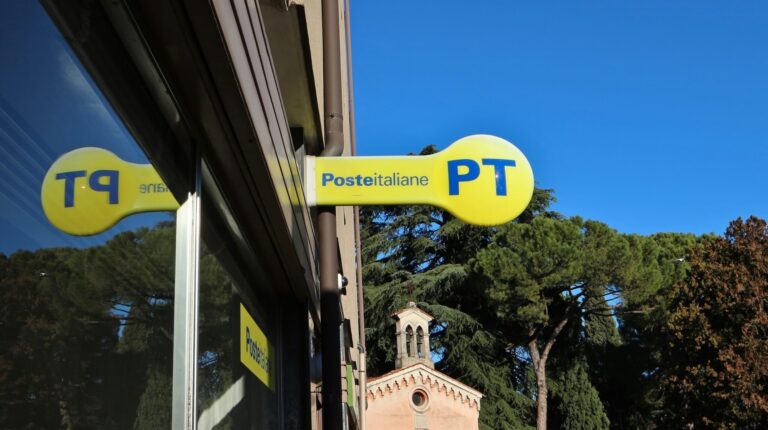 Poste Italiane sign hangs on the exterior or a post office on a sunny day.